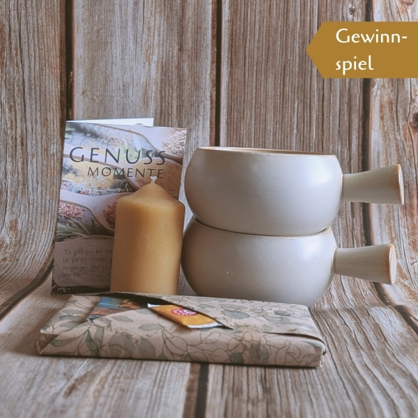 Gewinnspiel-Arrangement für den Newsletter mit zwei Tassen, einer Bienenwachskerze, einer Karte „Genuss-Momente“ und einem Präsent auf Holzhintergrund.