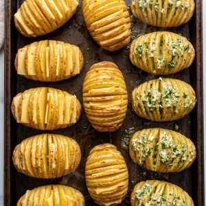 Draufsicht auf fächerartig eingeschnittene Hasselback-Kartoffeln, gefüllt mit Butter, Käse und Kräutern, auf einem Backblech.