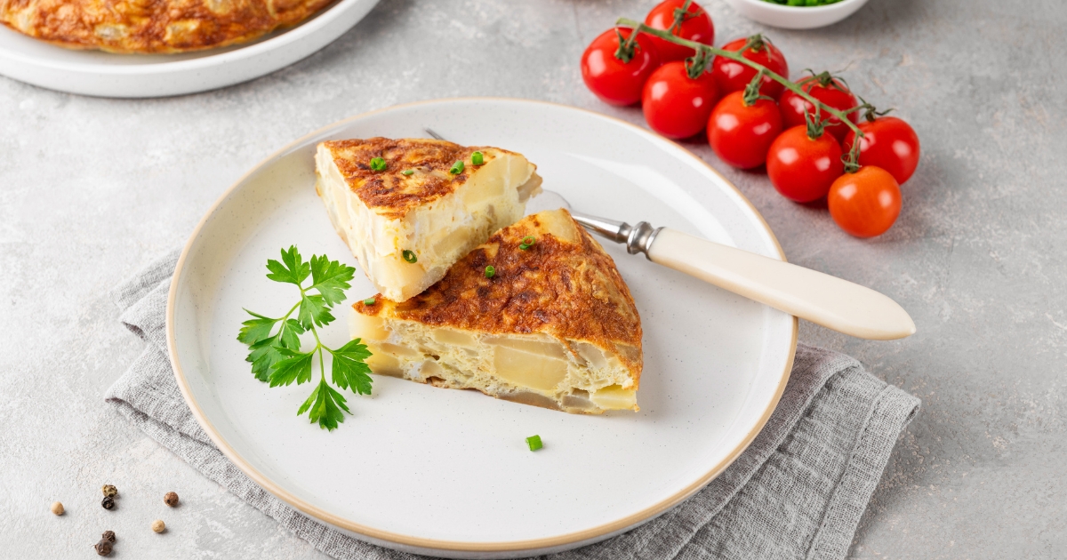 Zwei Stücke spanische Kartoffeltortilla angerichtet auf einem Teller mit Petersilie und Strauchtomaten.